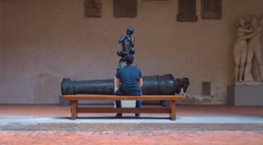 uomo seduto su un cannone che guarda una statua 